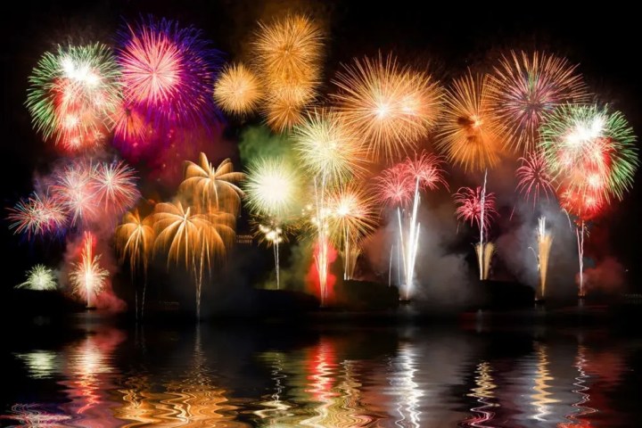 Colorful fireworks exploding over water at night, with reflections on the surface.